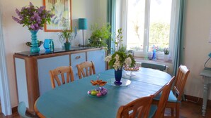 A dining area with a round table, chairs, a vase with flowers, a painting on the wall, and a window with curtains. - Country house with enclosed garden - Pets welcome (Barrais-Bussolles)