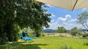 A garden with a pergola, two blue chairs, and a view of a hilly landscape.