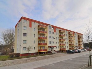 Un edificio residencial de varios pisos con balcones, una zona de estacionamiento y cielo despejado.
