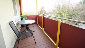 Un balcon avec une table et des chaises, un pot de fleurs et une vue sur des arbres et un immeuble.