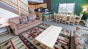 A spacious living area with a high wooden staircase, a kitchen with wooden cabinets, a dining area with wooden chairs, and a large window providing a view of the outdoors. - Continental Divide Cabin with breathtaking views from large picture windows (Estes Park)