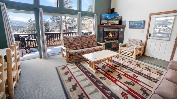 A spacious living room with a large window, a fireplace, and a cozy seating area. - Continental Divide Cabin with breathtaking views from large picture windows (Estes Park)