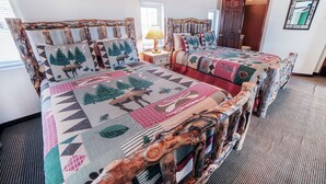 A bedroom with two wooden headboards, a large bed with a colorful quilt, a nightstand with a lamp, and a door leading to another room. - Continental Divide Cabin with breathtaking views from large picture windows (Estes Park)