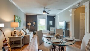 A dining area with a glass table, striped chairs, and a television in the background. - Music Row Condo in Spence Manor/Guitar Shaped Pool (Nashville)