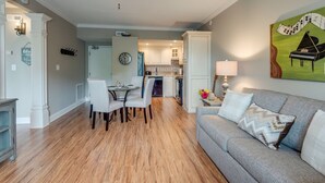 A dining area with a table and chairs, a kitchen in the background, and a living room with a couch and a painting. - Music Row Condo in Spence Manor/Guitar Shaped Pool (Nashville)
