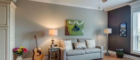 A living room with a grey sofa, a guitar, a lamp, and a ceiling fan.