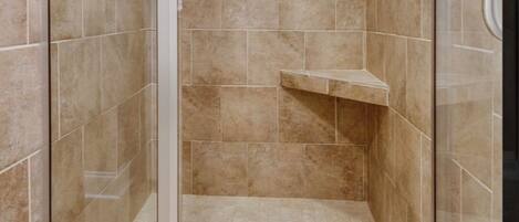A glass-enclosed shower with beige tiles, a built-in shelf, and a ceiling light.