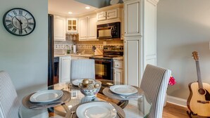 A dining area with a glass table set for four, surrounded by striped chairs. A clock is mounted on the wall to the left. - Music Row Condo in Spence Manor/Guitar Shaped Pool (Nashville)