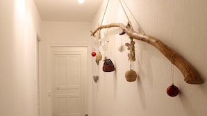 A hallway with a wooden branch wall hanging decorated with various ornaments. - Renovated countryside family cottage with garden (Cindré)