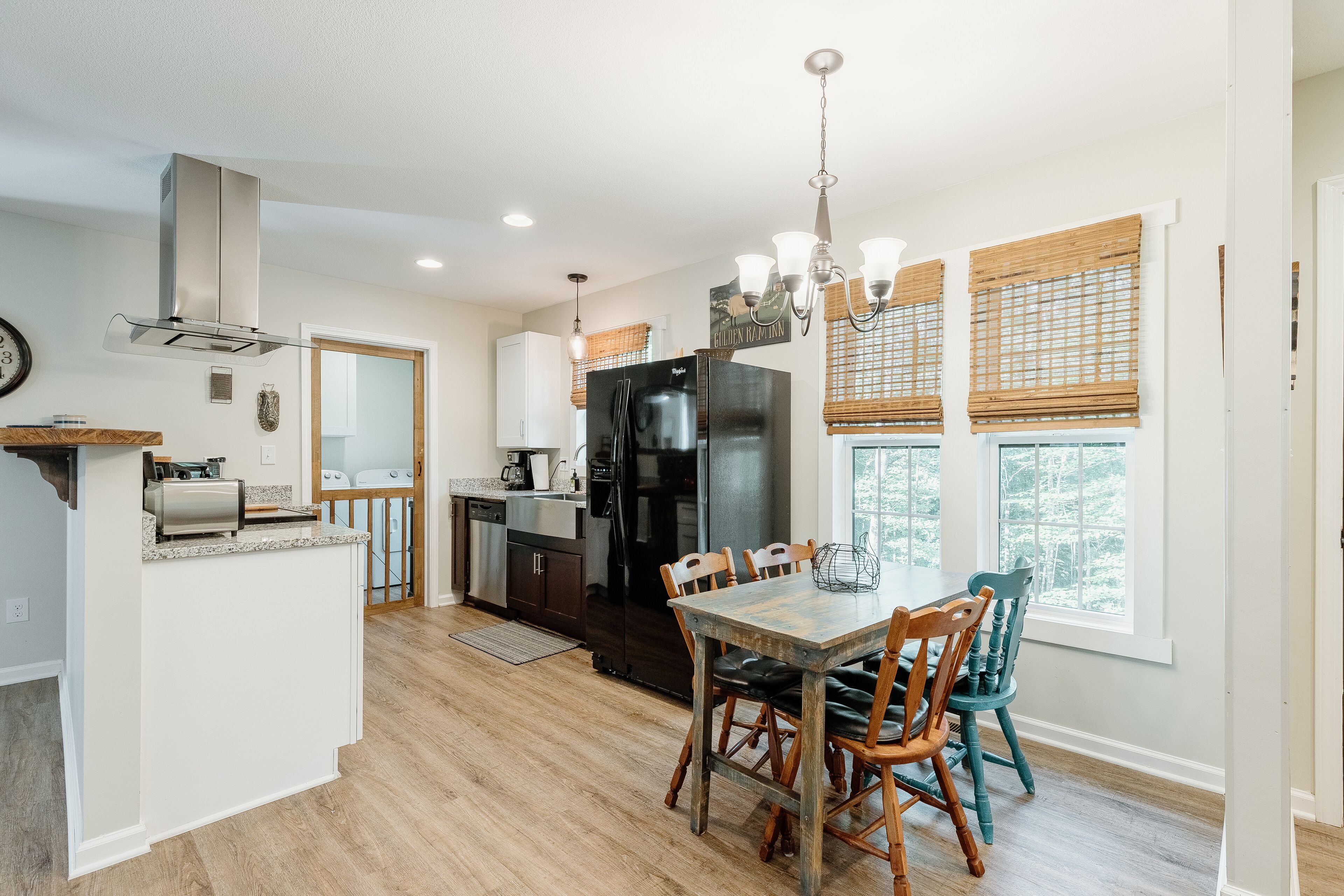 A modern kitchen with a central island, a dining area with wooden chairs, and a large refrigerator.