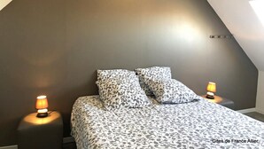 A bedroom with a sloped ceiling, two bedside lamps, a patterned bedspread, and a nightstand. - Renovated farmhouse with private pool and pets allowed (Échassières)
