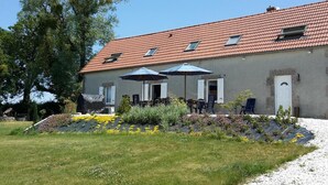 A two-story building with a tiled roof, a covered patio with outdoor seating, and a garden area with flowers and plants. - Renovated farmhouse with private pool and pets allowed (Échassières)