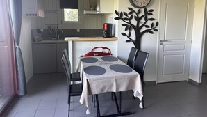 A compact kitchen with a dining area, a clock on the wall, and a door to the right. - Cottage with AC - 4 guests (Meillard)
