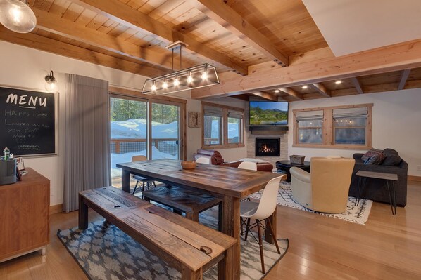 Une pièce spacieuse avec une table à manger en bois, des bancs, une cheminée et une grande fenêtre donnant sur un paysage enneigé.
