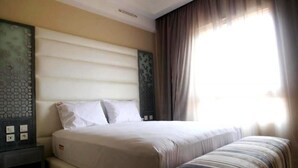 Een hotelkamer met een groot bed, nachtkastje en een raam met gordijnen.