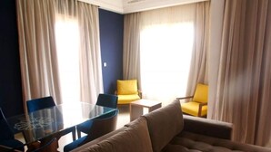 Een moderne hotelkamer met een bank, twee gele fauteuils, een glazen salontafel en een klein bijzettafeltje.