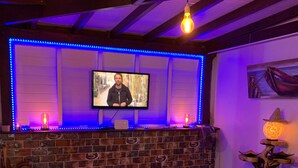 Een bar met een televisiescherm, blauwe LED-verlichting en een rustieke bakstenen muur.