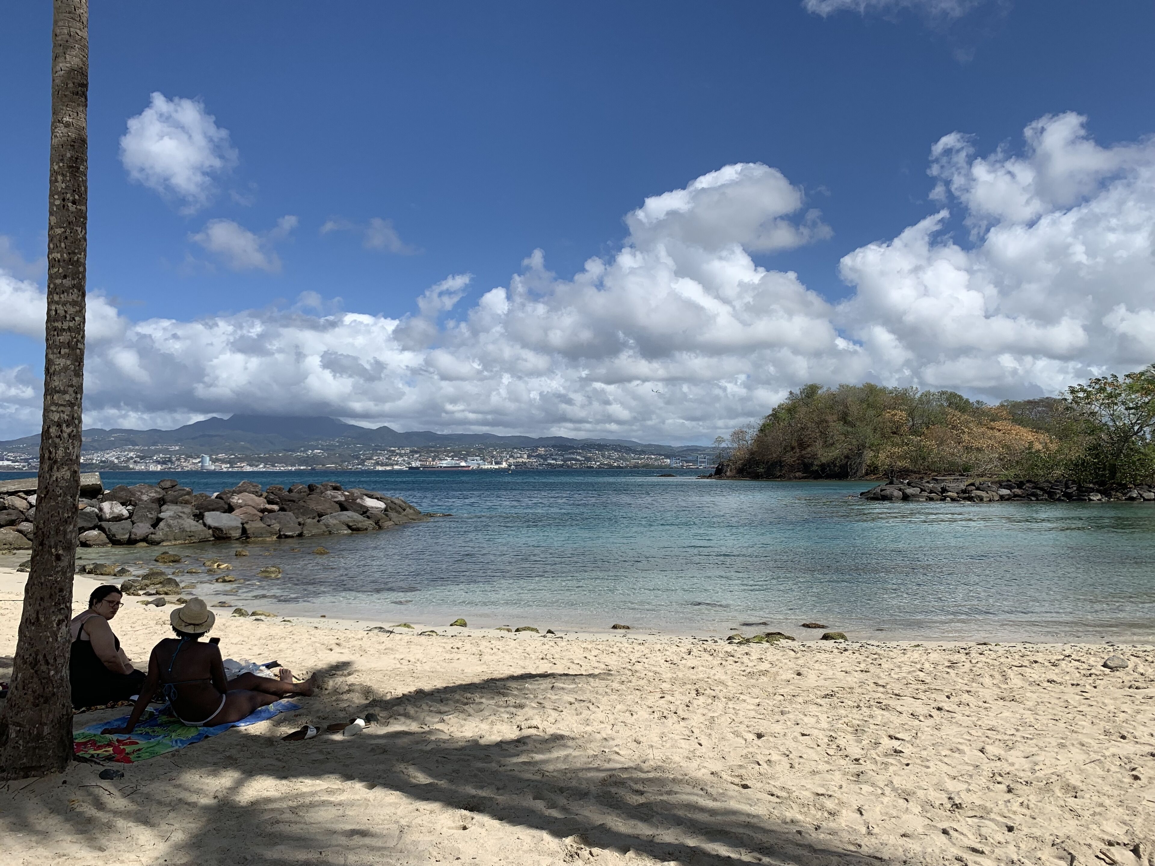 A beach with a clear view of the sea, a rocky shoreline, and a distant cityscape.