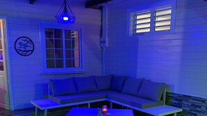 Een kamer met een blauw verlichte hoekbank, een tafeltje met een kaars, en een hanglamp.
