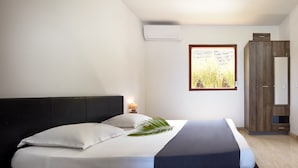 Een slaapkamer met een bed, nachtkastje, lamp, kast en een raam met uitzicht op hoog gras.