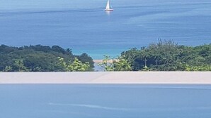 Een zeilboot op een rustige zee, met een strand en weelderige begroeiing op de voorgrond.