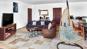 Een woonkamer met een bank, een televisie, een hangstoel en een keukenhoek.