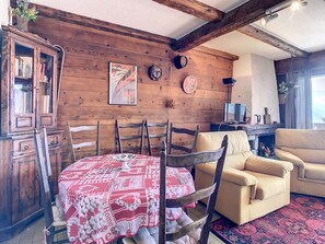 A cozy living room with a wooden wall, a dining table with a red and white tablecloth, a beige sofa, and a television on a wooden stand.