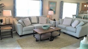 A living room with two light-colored sofas, a wooden coffee table, and a small side table with a lamp. - Close to Fun, Villa In Walking distance to Lake Sumter Landing w/Golf Cart! (The Villages)