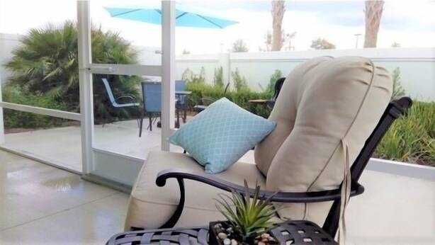 A beige cushioned chair with a blue pillow, a small potted plant, and a black metal table. - Close to Fun, Villa In Walking distance to Lake Sumter Landing w/Golf Cart! (The Villages)