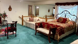 Ett sovrum med en stor säng, en soffa, en trästol, ett litet bord med en vas med blommor och en trappa.