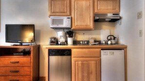 Eine kleine Küche mit Holzausstattung, einer Mikrowelle, einem Toaster, einer Kaffeemaschine, einem Wasserkocher und einem Geschirrspüler.