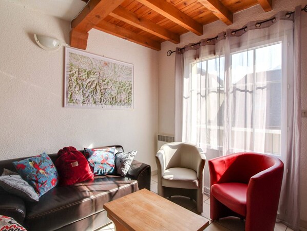 Un salon avec un plafond en bois, un canapé agrémenté de coussins colorés, un fauteuil rouge et une table basse.
