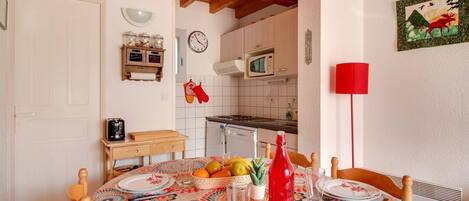 A dining area with a wooden table set for four, a clock, and a kitchen in the background.