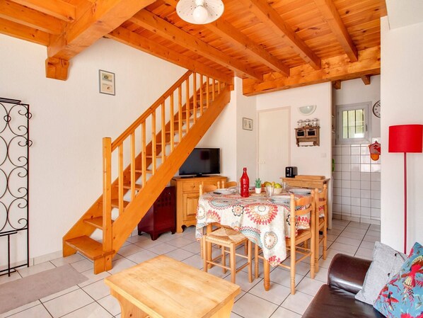 Ein gemütliches Wohnzimmer mit einer Holztreppe, einem Essbereich mit Tisch für vier Personen und einer im Hintergrund sichtbaren Küche.