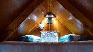 Un dormitorio acogedor en el ático con techo inclinado, una cama con edredón blanco, dos almohadas y una lámpara colgante.