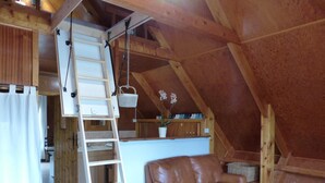 Un cuarto ático acogedor con techo de madera, un sofá de cuero marrón, una escalera pequeña y una mesa con tazas.