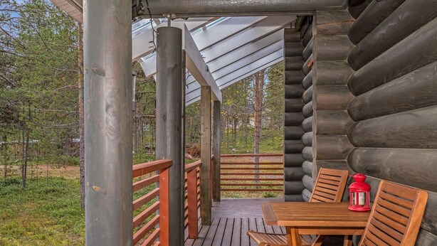 A wooden deck with a table and chairs, a red lantern, and a view of a forested area.