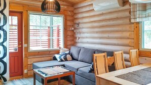 A log cabin interior with a sofa, dining table, chairs, and a window with blinds.