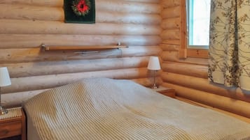 Une chambre de cabane en bois comprenant un lit, des lampes de chevet, une fenêtre avec des rideaux et une étagère fixée au mur.
