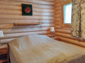 Une chambre de cabane en bois comprenant un lit, des lampes de chevet, une fenêtre avec des rideaux et une étagère fixée au mur.