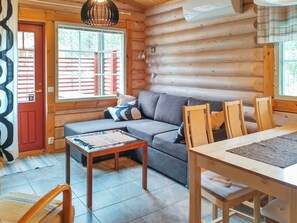 A log cabin interior with a sofa, dining table, chairs, and a hanging light fixture.