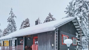 A log cabin with a snow-covered roof, a red door, and a porch with outdoor seating.