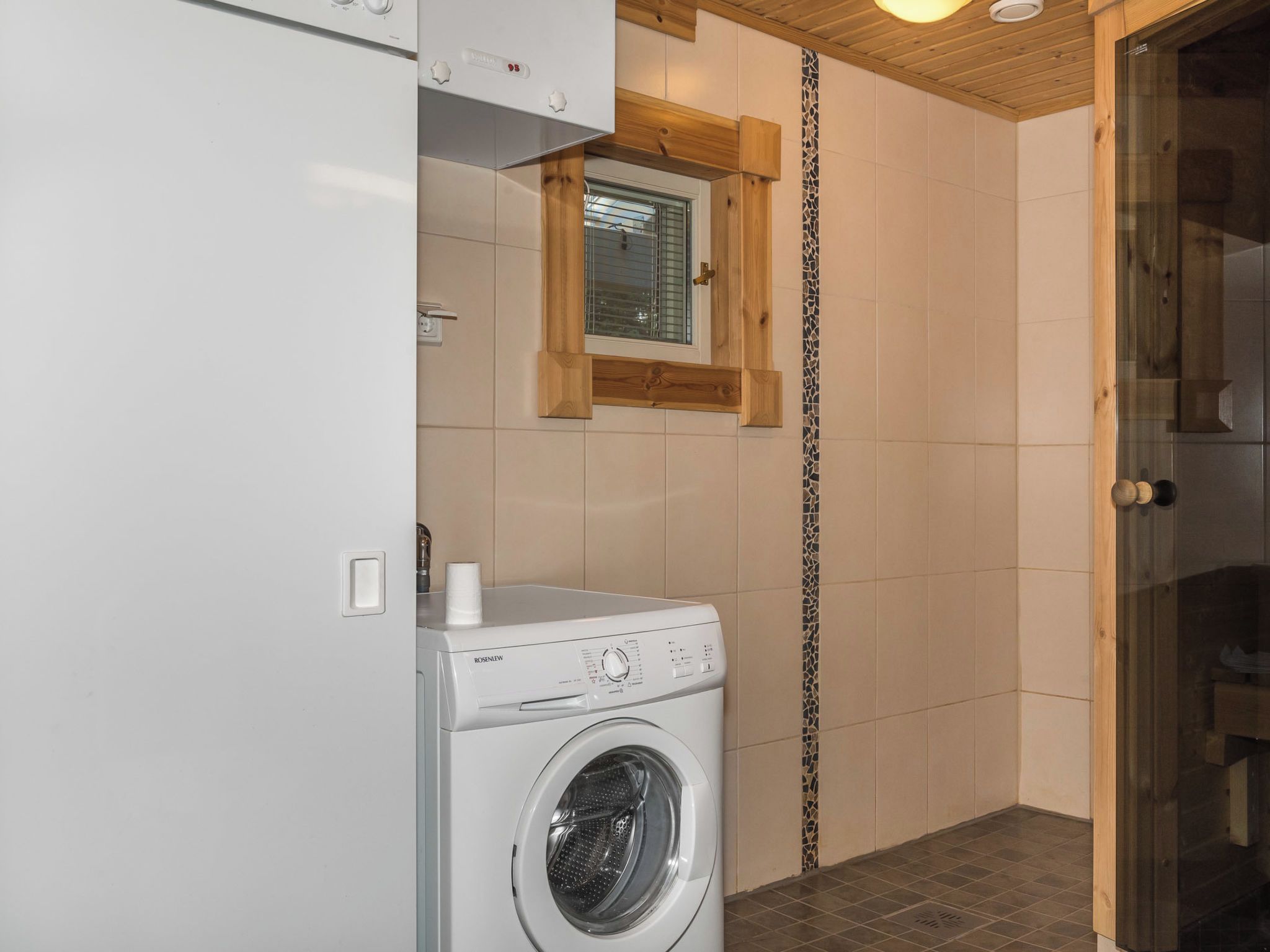 A compact laundry room with a front-loading washing machine, a small window, and wooden accents on the walls.