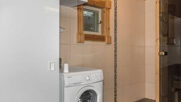 A compact laundry room with a front-loading washing machine, a small window, and wooden accents on the walls.