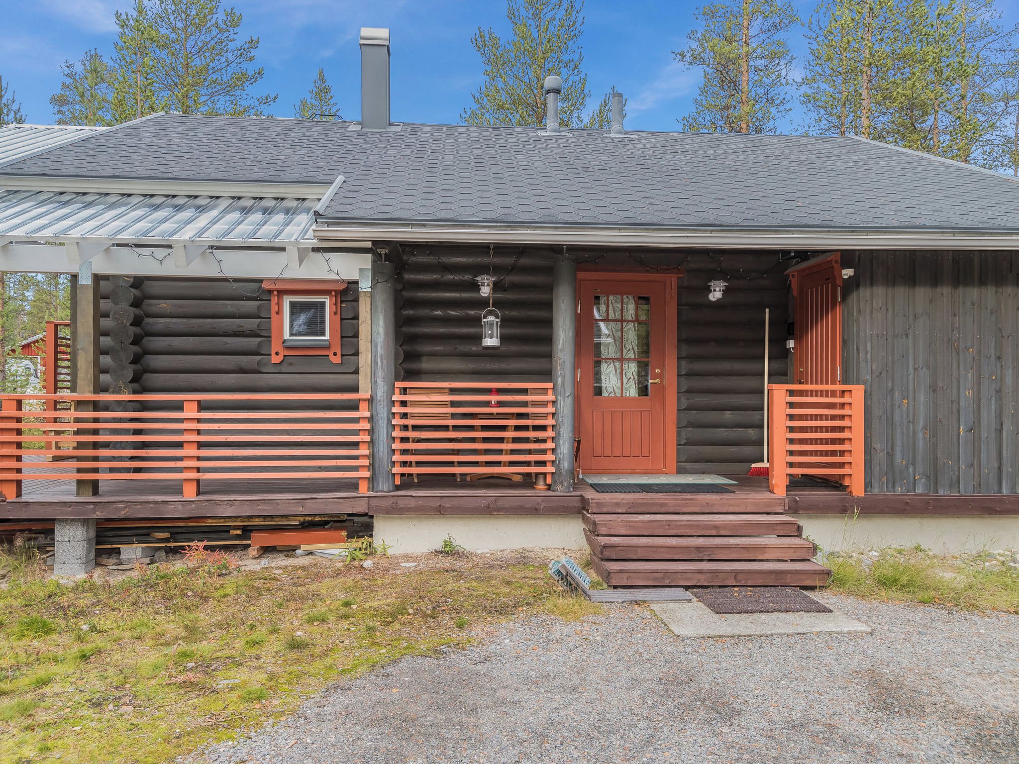 A log cabin with a porch, a red door, and a chimney.