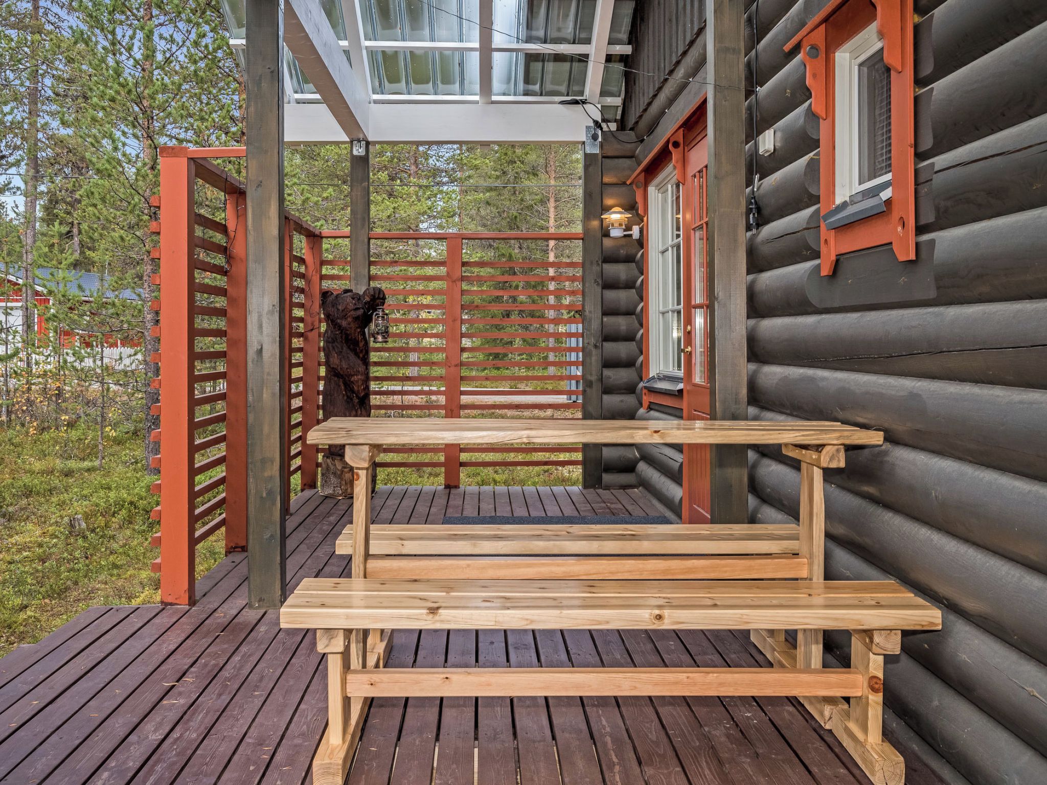 A wooden deck with a bench, a bear sculpture, and a glass-enclosed upper level.