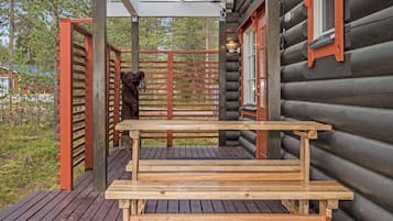 Une terrasse en bois avec un banc, une sculpture d’ours et un niveau supérieur fermé par des vitres.