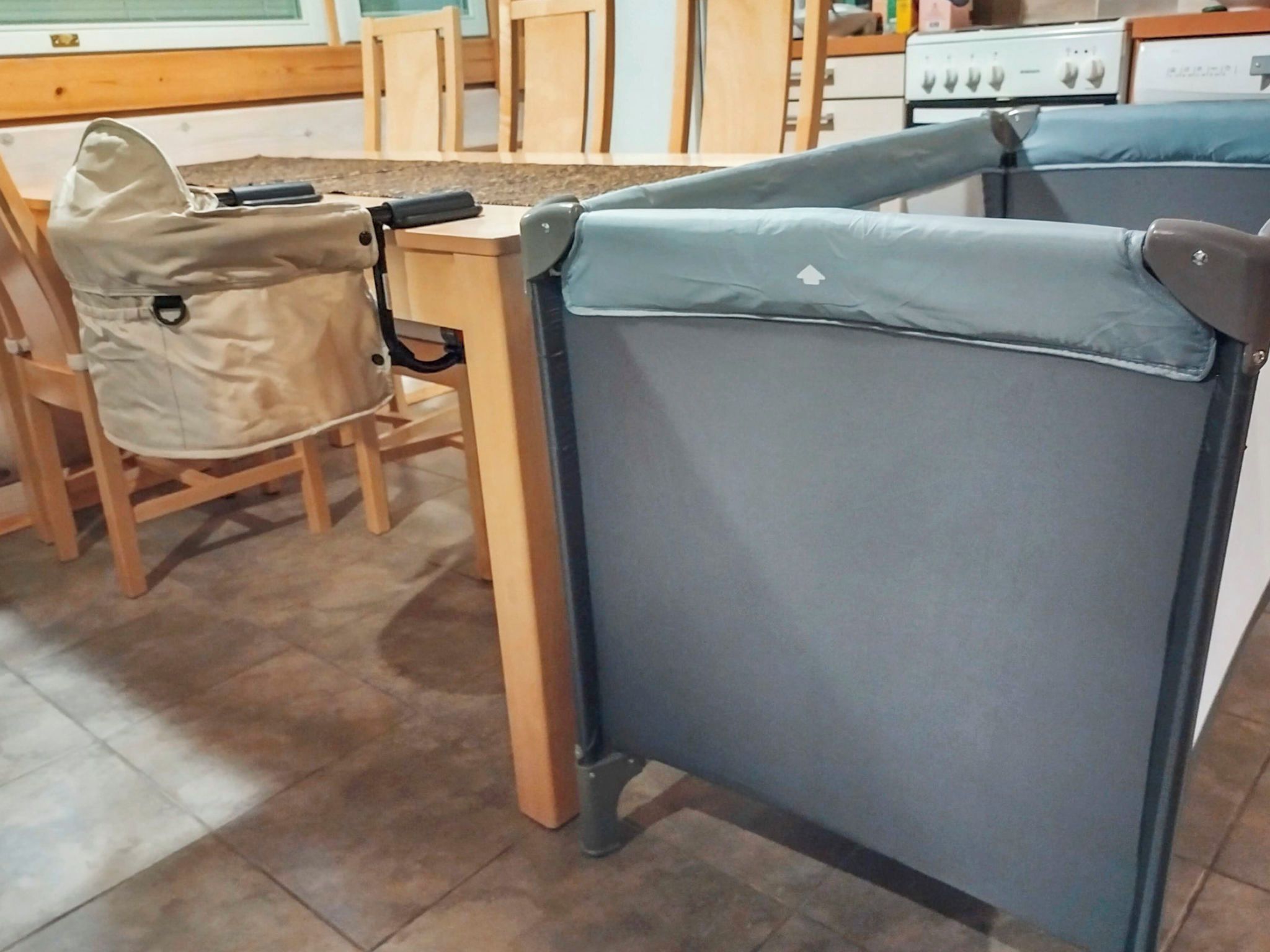 Une pièce avec une table pliante et une chaise, un poêle en arrière-plan et un sol carrelé.
