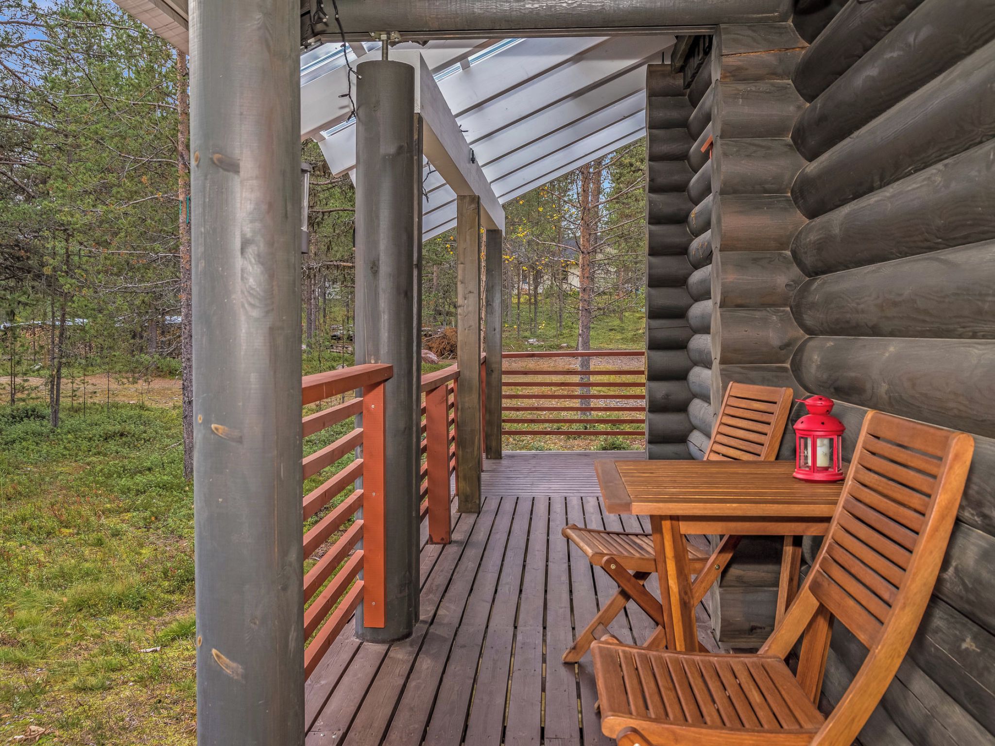 Une terrasse en bois avec une table et des chaises, une lanterne rouge et une vue sur une zone boisée.