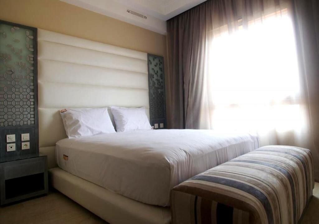 A hotel room with a large bed, a bedside table, and a window with curtains.
